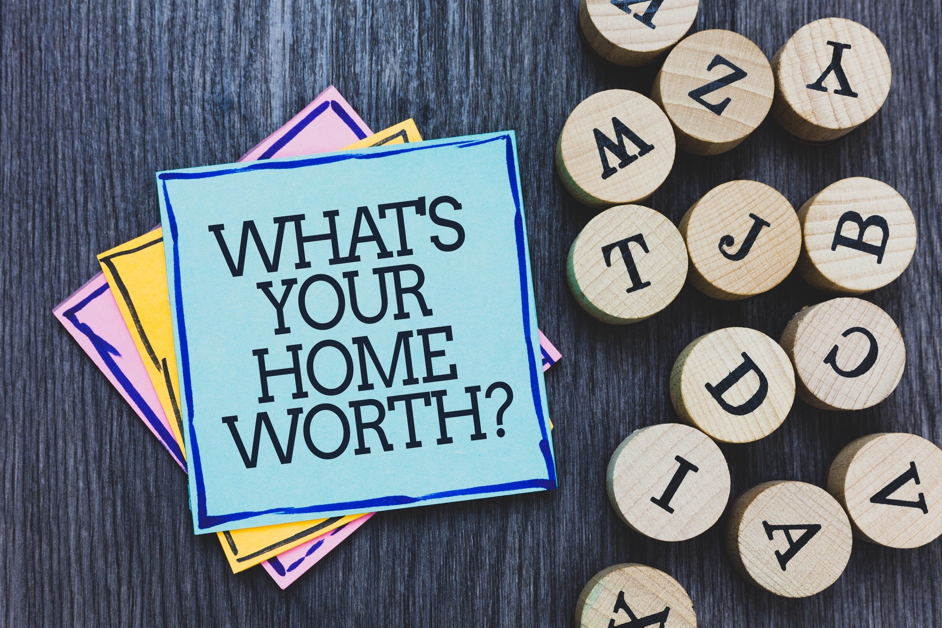 Handwriting text What s is Your Home Worth question. Concept meaning Value of a house Property Cost Price Rate Black wooden deck written sticky note beside some round woody alphabets.